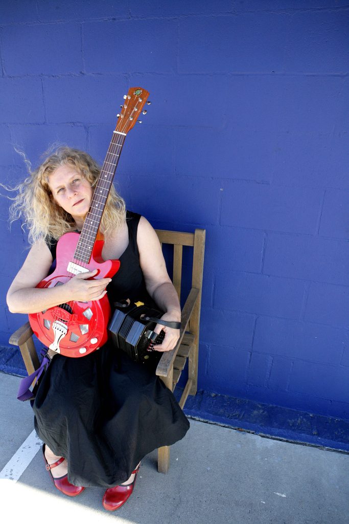 Kristina Olsen sitting with red shoes and red guitar